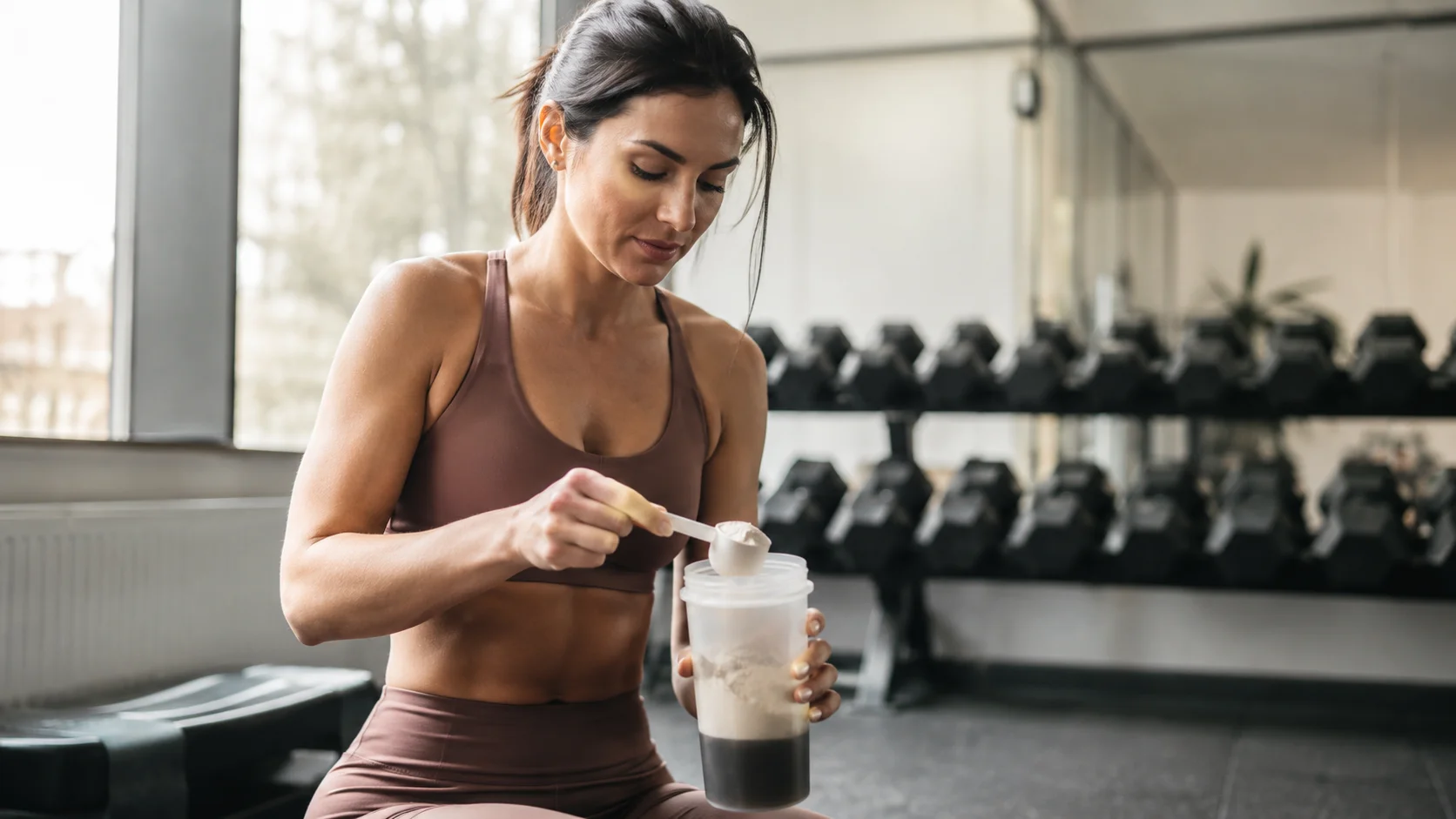 Kvinde der blander kreatinpulver i en shaker i fitnesscenteret